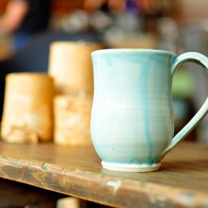 A handmade, wheel-thrown mug dipped in teal glaze with drip lines.