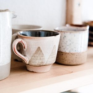 A handmade, wheel-thrown brown mug with triangle accents and a tapered bottom.