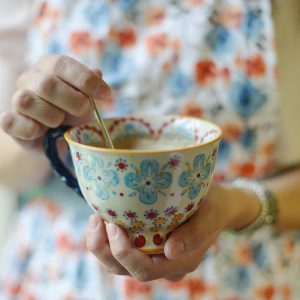 A handmade, wheel-thrown mug with colorful floral accents and a tapered bottom.